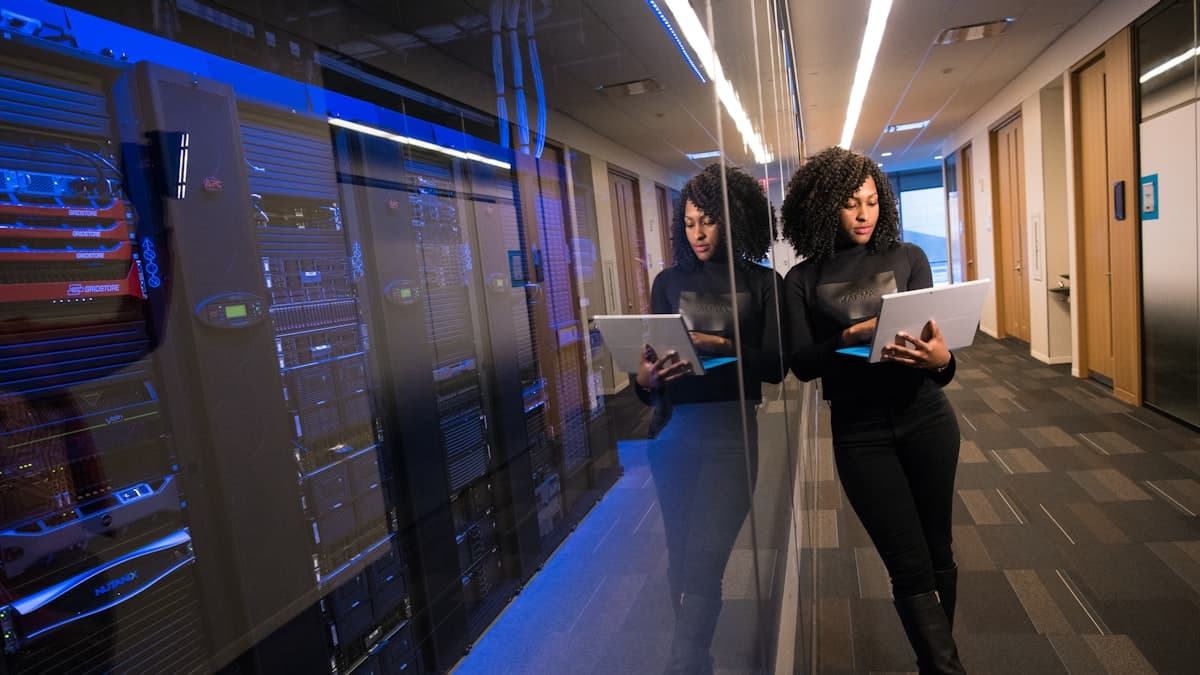 IT professional reviewing infrastructure on a laptop beside a blue-lit server room