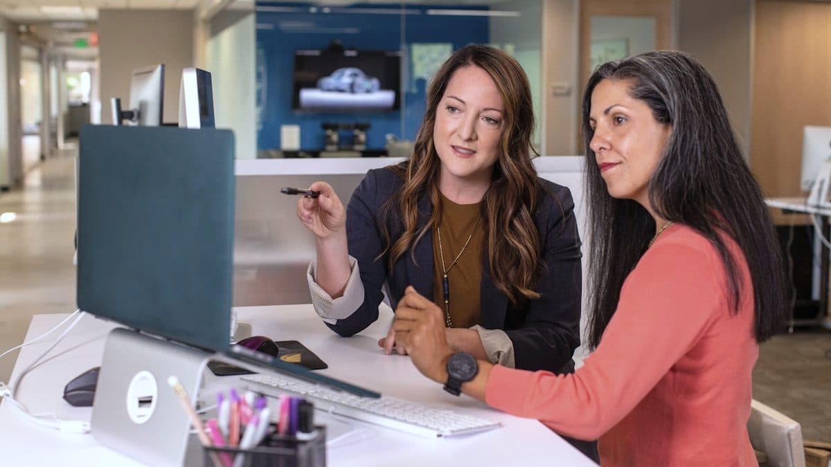 Two colleagues reviewing customer records together at a desktop screen in a modern office