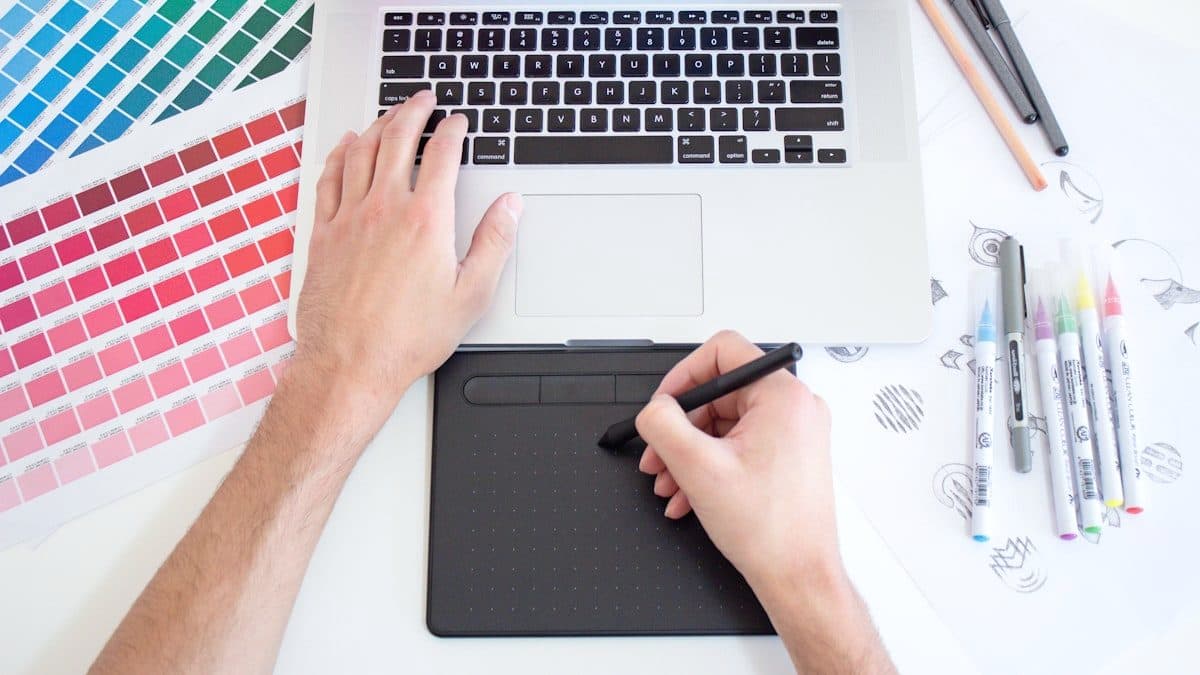 Designer sketching on a graphics tablet beside printed colour swatch fans