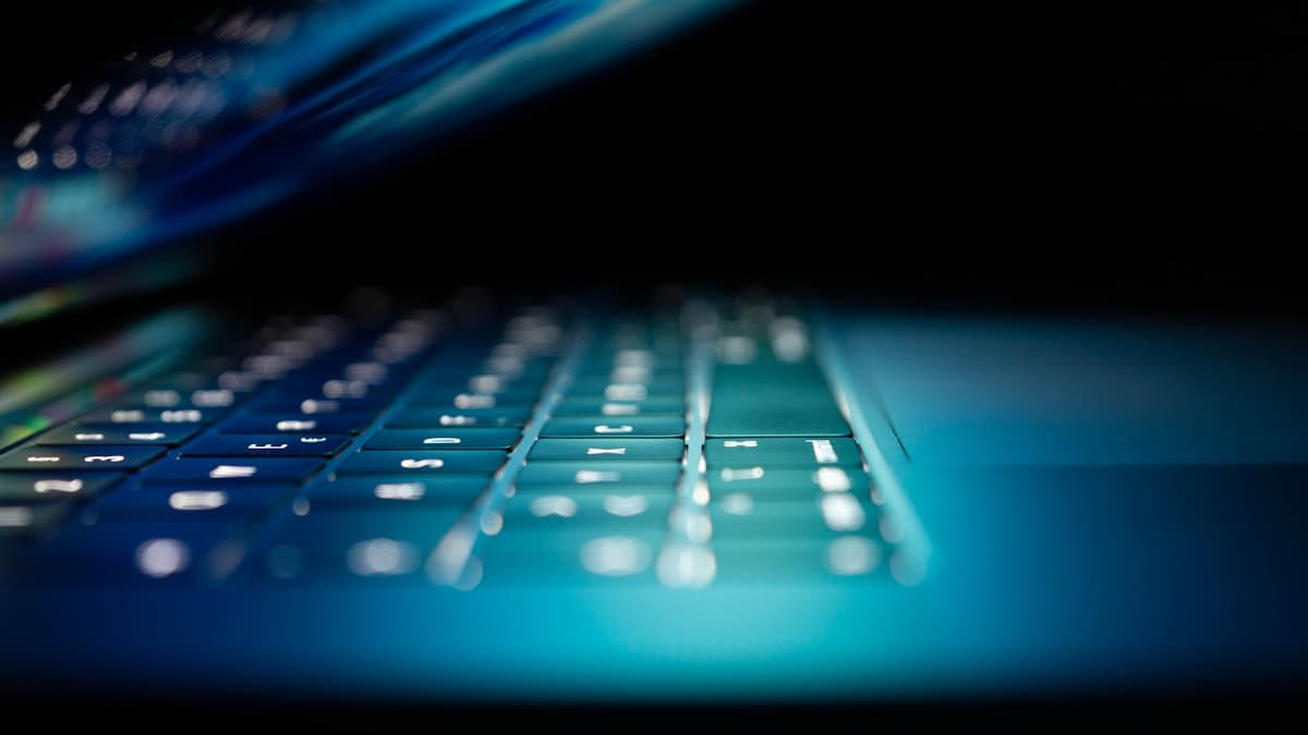 Backlit laptop keyboard glowing blue in a darkened room during a remote login