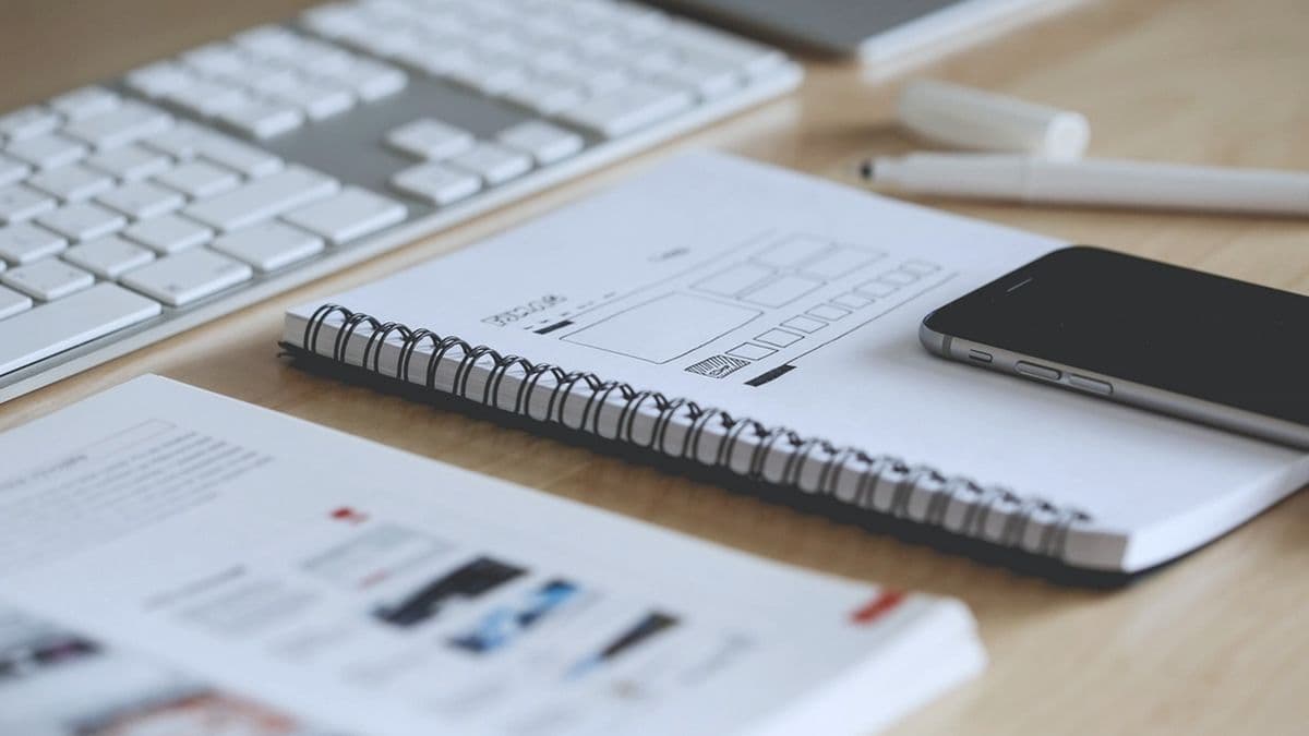 Interface wireframes sketched in a notebook beside a keyboard and phone